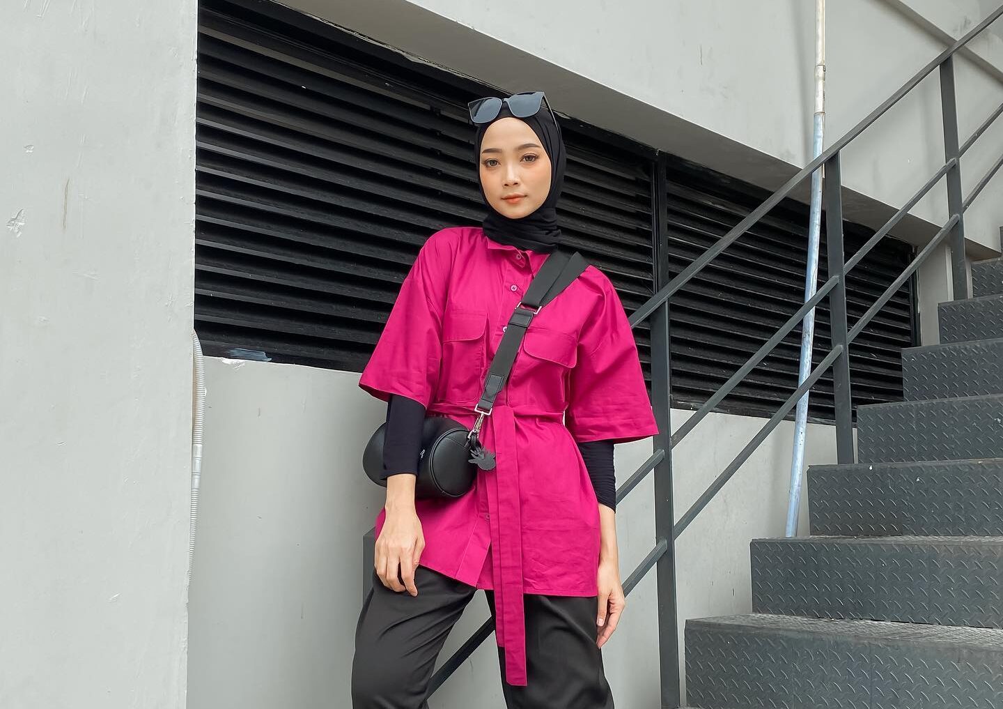 Wanita Indonesia mengenakan jilbab hitam di atas pakaian merah muda atau fuchsia.